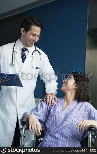 Young smiling female patient sitting in a wheelchair, looking up at doctor standing beside her