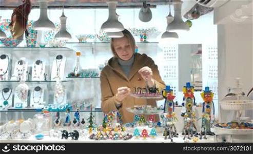 Young smiling female tourist choosing souvenirs in Venetian store of glassware and masks