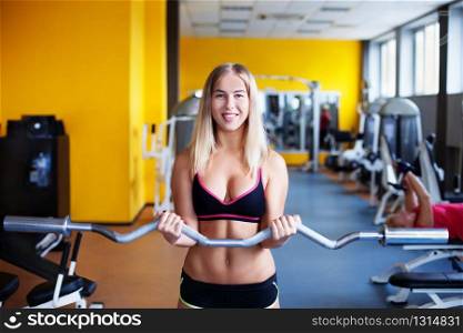 Young smiling girl in the gym with bar. Girl in the gym