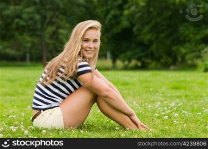 Young smiling girl sitting on the park and looking toward the camera