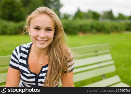 Young smiling girl sitting on the park chair with very narrow depth of field and focus on the eyes