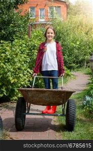 Young smiling girl with wheelbarrow working at garden at sunny day