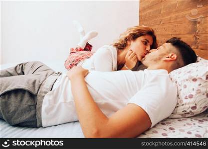 Young smiling heterosexual couple lying down together on the bed kissing