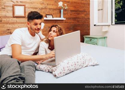 Young smiling heterosexual couple lying down together on the bed using a laptop