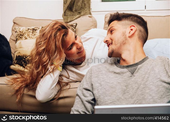 Young smiling heterosexual couple together on sofa using a laptop