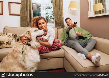 Young smiling heterosexual couple together on sofa with their dog drinking from a cup