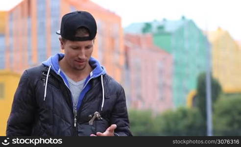 Young smiling hipster catching set of house keys and doing a victory gesture against blurred modern building background