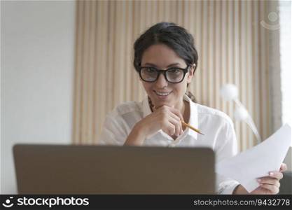 Young smiling italian business woman wearing glasses using laptop at work, happy female employee looking at screen with smile, reading email with good news while working online on computer home office. Happy female employee looking at laptop screen with smile, reading email with good news at work