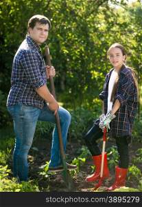 Young smiling man and cute girl digging soil at garden with shovels