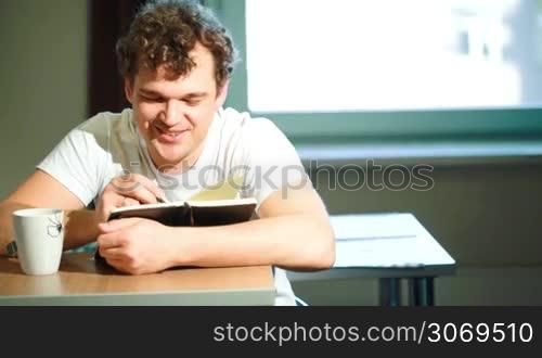 Young smiling man at home taking notes and drinking tea