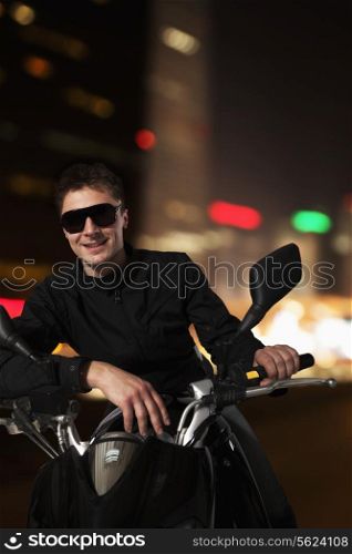 Young smiling man in sunglasses sitting on his motorcycle at night in Beijing