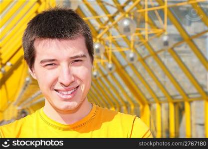 young smiling man in yellow shirt on footbridge