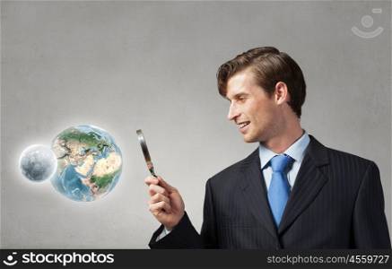 Young smiling man looking in magnifying glass. Elements of this image are furnished by NASA. Man with magnifier