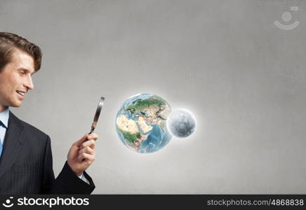 Young smiling man looking in magnifying glass. Elements of this image are furnished by NASA. Man with magnifier