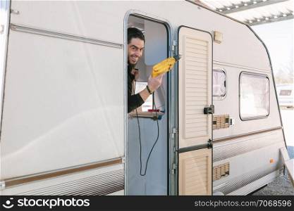 Young smiling man with a drill restoring his old caravan