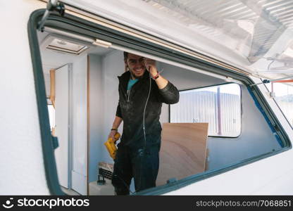 Young smiling man with a drill restoring his old caravan