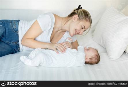 Young smiling mother playing on bed with her cute baby boy