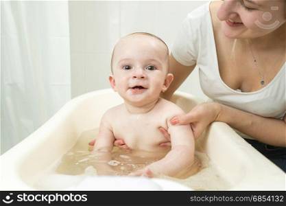 Young smiling mother washing her cute baby in plastic bath