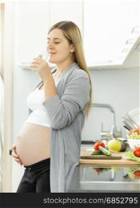 Young smiling pregnant woman drinking water on kitchen