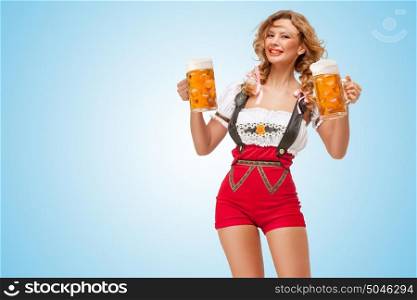 Young smiling sexy Swiss woman wearing red jumper shorts with suspenders in a form of a traditional dirndl, holding two beer mugs on blue background.