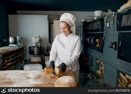 Young smiling woman baker chef holding knife and cutting fresh bread on wooden table. Healthy eating and traditional bakery concept. Baker chef holding knife and cutting fresh bread on wooden table