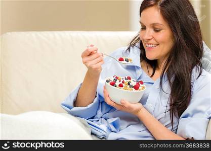 Young smiling woman eating healthy cereal lying on couch