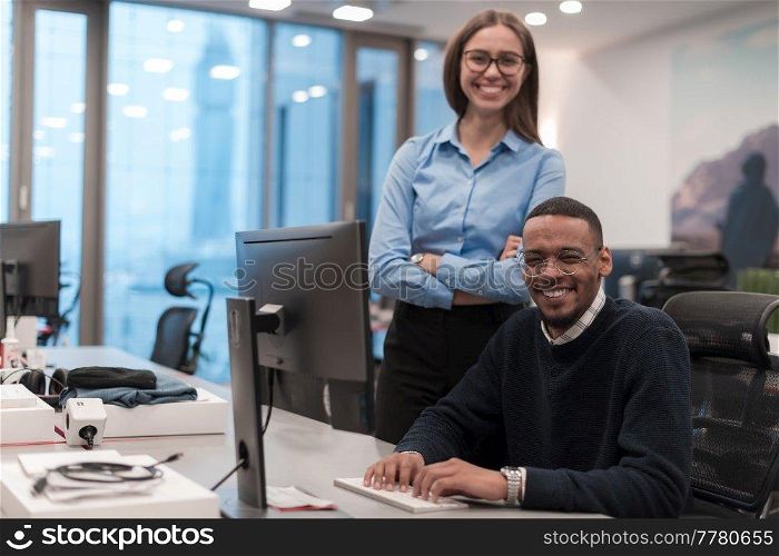 Young smiling woman explaining to serious African American coworker project strategy. Diverse startup coworkers students woman and man talking discussing working in modern office using the computer. High-quality photo. Young smiling woman explaining to serious African American coworker project strategy. Diverse startup coworkers students woman and man talking discussing working in modern office using computer.
