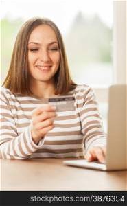 Young smiling woman holding a credit card in her hand while doing online shopping at home