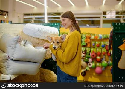 Young smiling woman holding corgi dog on hands choosing soft s≤eπng place at pet shop. Young woman holding corgi dog on hands choosing s≤eπng place at pet shop