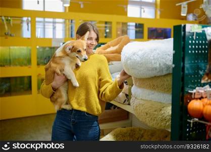 Young smiling woman holding corgi dog on hands choosing soft sleeping place at pet shop. Young woman holding corgi dog on hands choosing sleeping place at pet shop