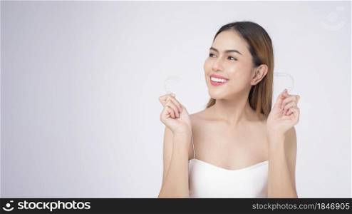 Young smiling woman holding invisalign braces in studio, dental healthcare and Orthodontic concept