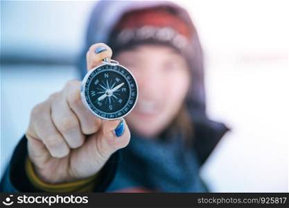 Young smiling woman holds up a compass. Wintertime, gloves and hood.