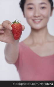 Young smiling woman in pink shirt holding and showing a strawberry