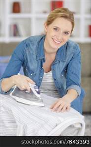 young smiling woman ironing clothes on ironing board at home