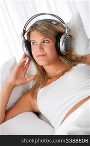Young smiling woman listening to music with headphones on white sofa