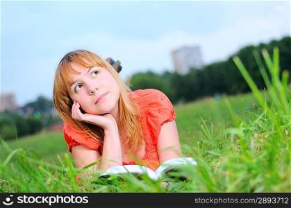Young smiling woman lying in field and dreaming with book in her hands