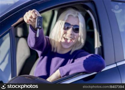 Young smiling woman seated in her new car showing the car key. Focus on the key