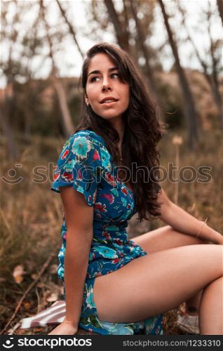 Young smiling woman squatting in the forest wearing a dress