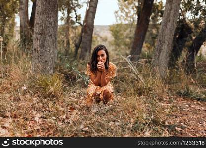 Young smiling woman squatting in the forest wearing a dress