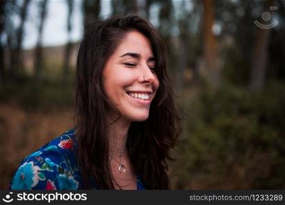 Young smiling woman wearing dress in the forest with closed eyes