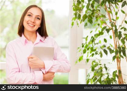 Young smiling woman with a pink shirt standing with a tablet pc in her hands