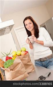 Young smiling woman with groceries drinking cup of coffee