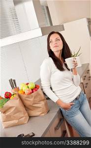 Young smiling woman with groceries drinking cup of coffee in the kitchen