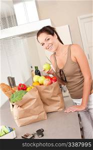 Young smiling woman with groceries holding apple