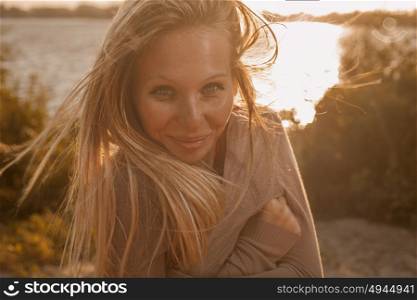 Young smiling woman with long blond hair posing on summer beach with sun behind. Young smiling woman with long blond hair posing on summer beach with sun behind retro color image full of warm sunshine