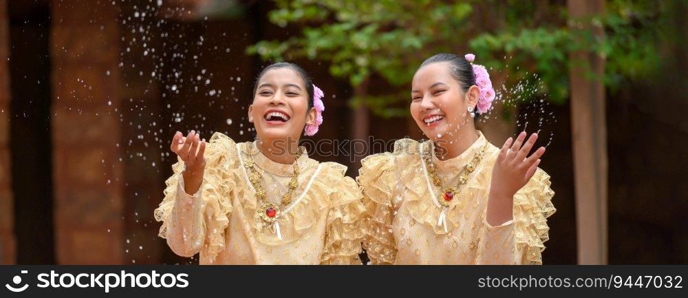 Young smiling women dress in beautiful Thai costumes splashing water in temples and preserve the good culture of Thai people during Songkran festival. Thai New Year, Family Day in April