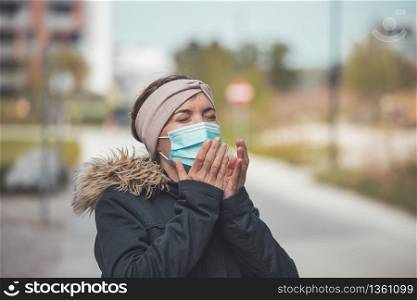 Young sneezing woman outdoors wearing a face mask. Corona and flu season.