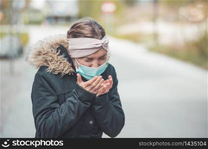 Young sneezing woman outdoors wearing a face mask. Corona and flu season.