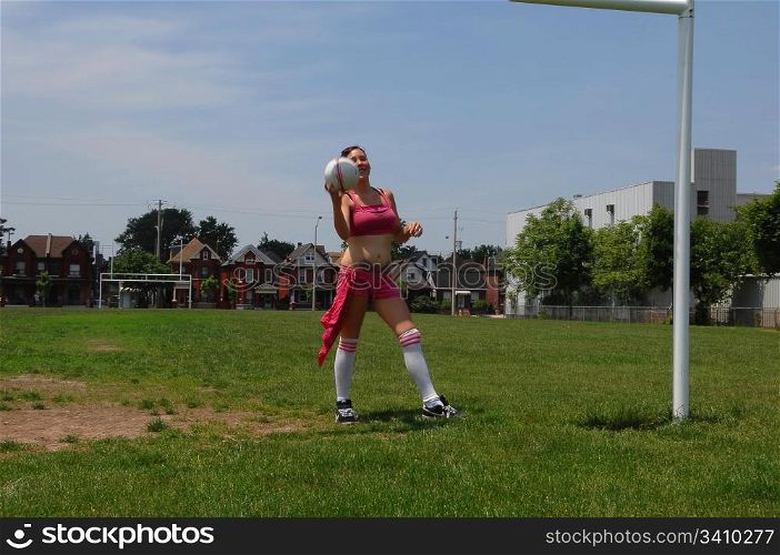 Young soccer girl on a soccer field in an pink shorts and top training some tricks with the soccer ball.