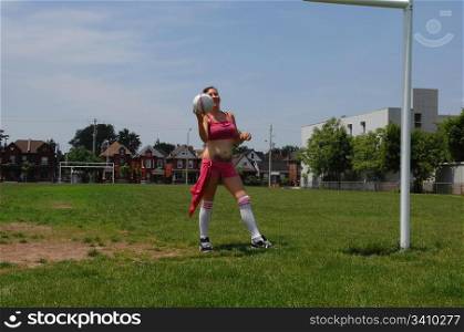 Young soccer girl on a soccer field in an pink shorts and top training some tricks with the soccer ball.